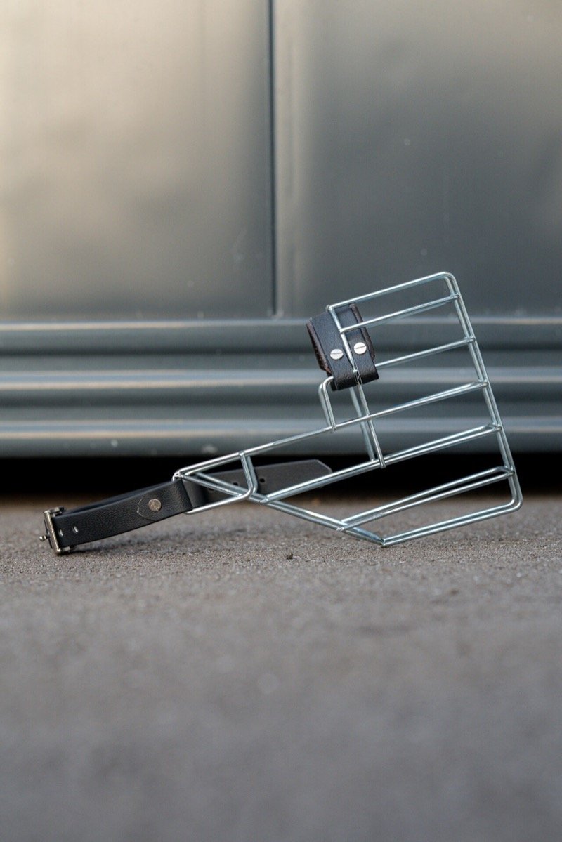 A wire basket muzzle with leather straps lying on the ground